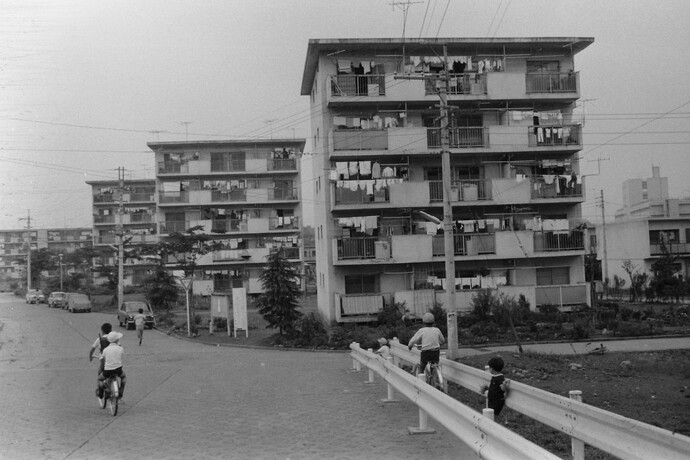 写真：昭和45年の野塩団地、並ぶ団地の建物の背景に子供たちが自転車に乗っている