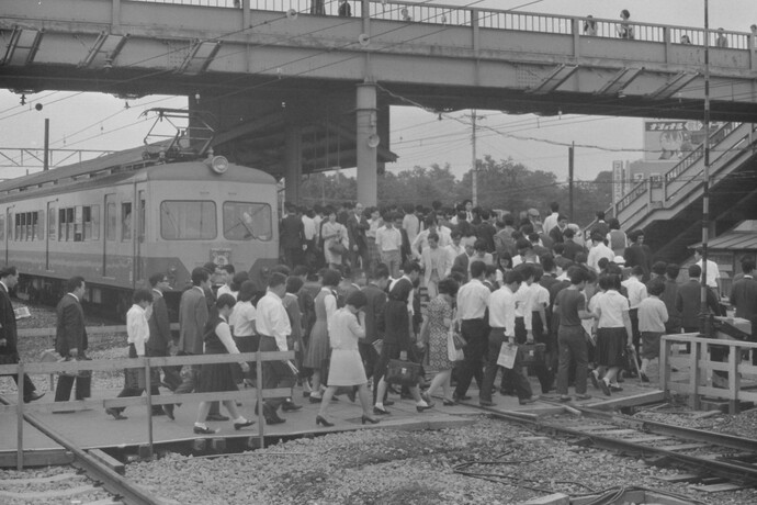 写真：昭和45年の清瀬駅、構内の踏切を渡って池袋行の電車がとまるホームへ向かう多くの通勤通学客、駅の上には陸橋がかかっている